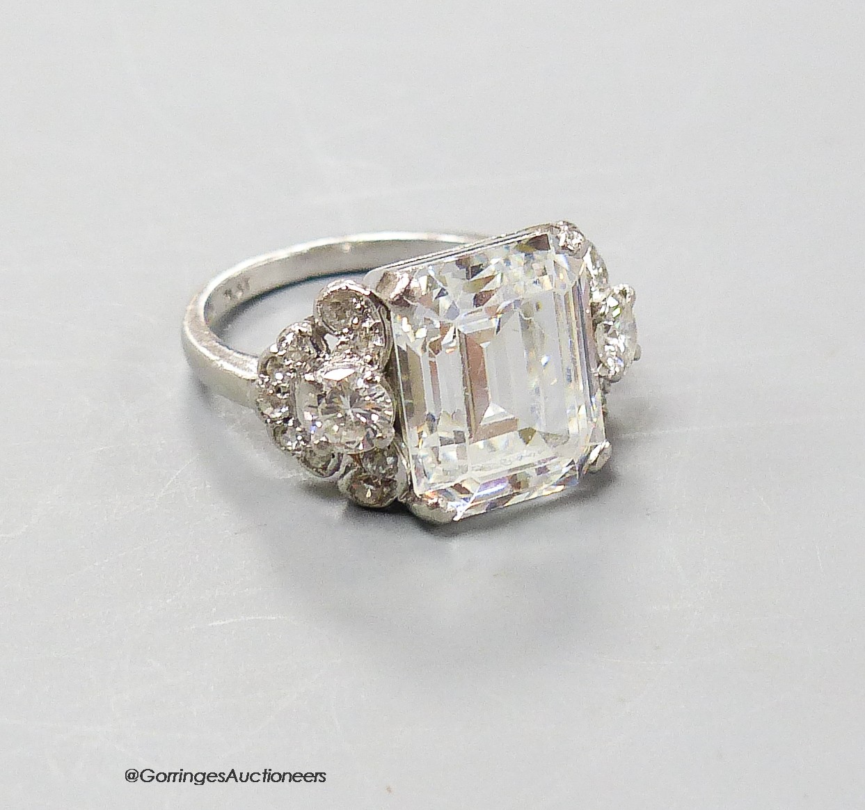 A platinum and emerald cut simulated diamond dress ring, with diamond cluster set shoulders, size F, gross 6.5 grams.